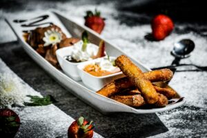 Fried churros served alongside a creamy dip and fresh strawberries.